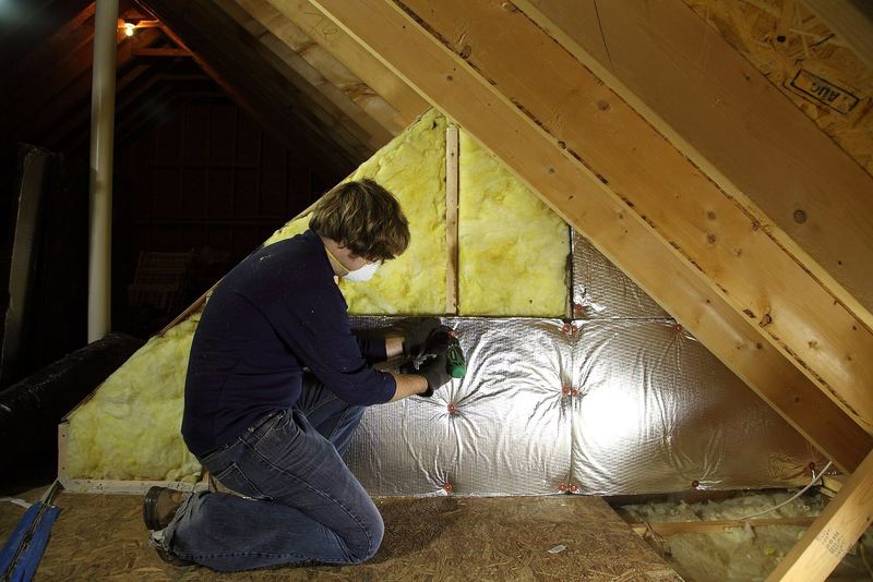 A person kneeling between roof timbers in a loft space, working on insulation
