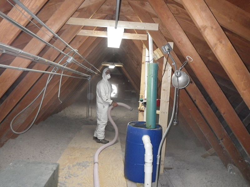 A worker in a white protective suit in a long, narrow roof space
