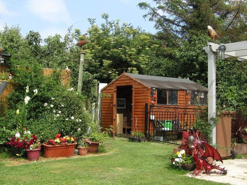 A garden with a timber shed, lawn and dense planting